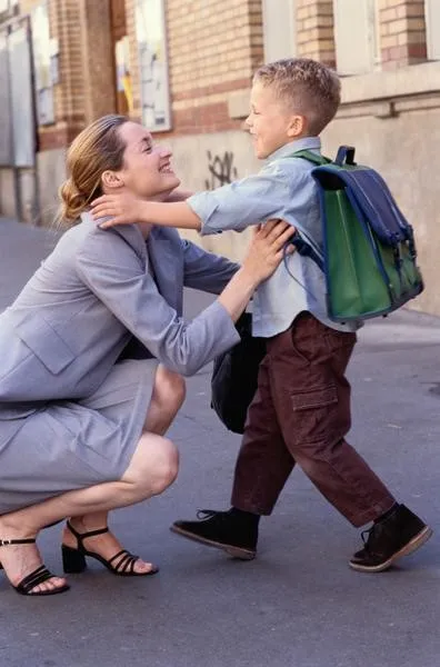 A child with a backpack greeting a parent outside school